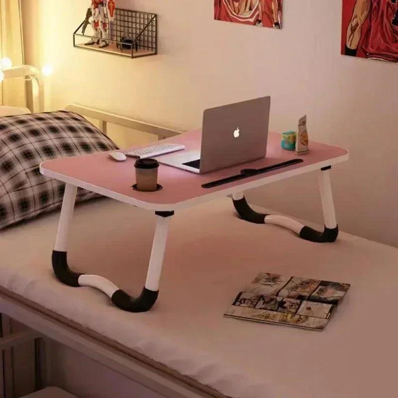 Pink portable laptop desk with foldable legs placed on a bed for working from home