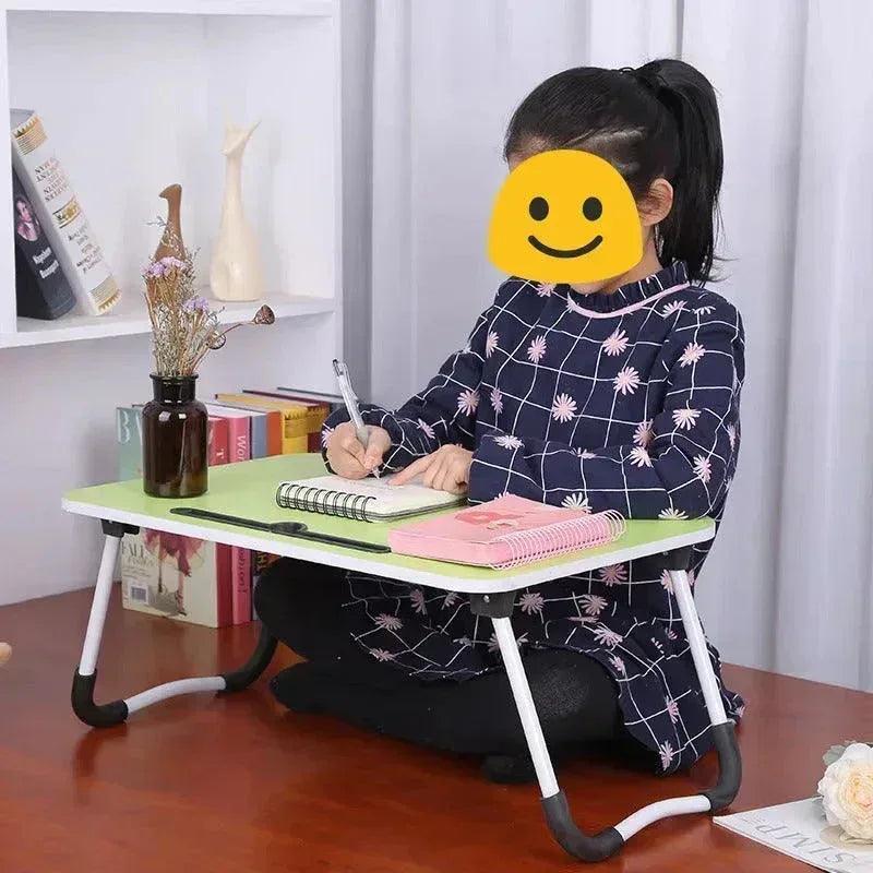 Young girl sitting on the floor writing in a notebook on a portable folding study table